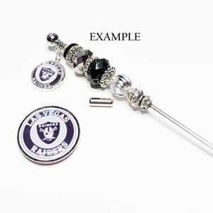 May include: A decorative silver-toned bead and charm accessory with black and silver beads. The charm features the Las Vegas Raiders logo. The word "EXAMPLE" is printed in black.