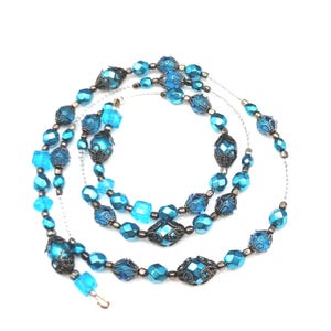 May include: A multi-strand necklace featuring various shades of blue beads. The necklace includes faceted, square, and ornate beads with a silver-tone chain and clasp. The beads are arranged in a layered design, creating a visually appealing accessory.