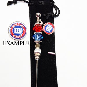 May include: A decorative pin featuring a New York Giants logo, red and blue beads, and silver detailing. The pin is shown with a small round logo and the word "EXAMPLE".