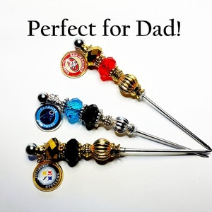 May include: Three decorative skewers with beaded accents and team logo charms. The skewers feature red, blue, and black beads, with charms for the San Francisco 49ers, Carolina Panthers, and Pittsburgh Steelers.