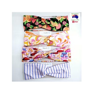 May include: Four colourful headbands with different patterns. The top headband has a tropical fruit print, the second headband has a pink and orange swirl pattern, the third headband has a mushroom print, and the bottom headband has a pink and blue striped pattern.