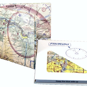 May include: A white box with the text "FliteWallet" and "Keep the blue side up" printed on it. The box contains a clear plastic window that shows a section of an aeronautical chart. The chart is folded into a wallet-like shape and is made of paper.