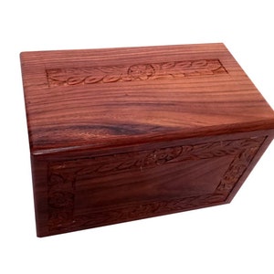 May include: A dark red wooden box with intricate floral carvings on the top and sides. The box has a hinged lid and is made of solid wood.