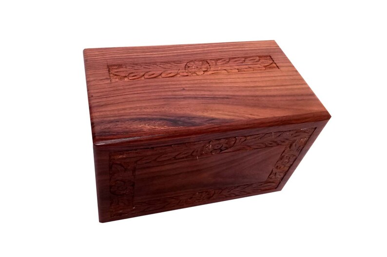 May include: A dark red wooden box with intricate floral carvings on the top and sides. The box has a hinged lid and is made of solid wood.