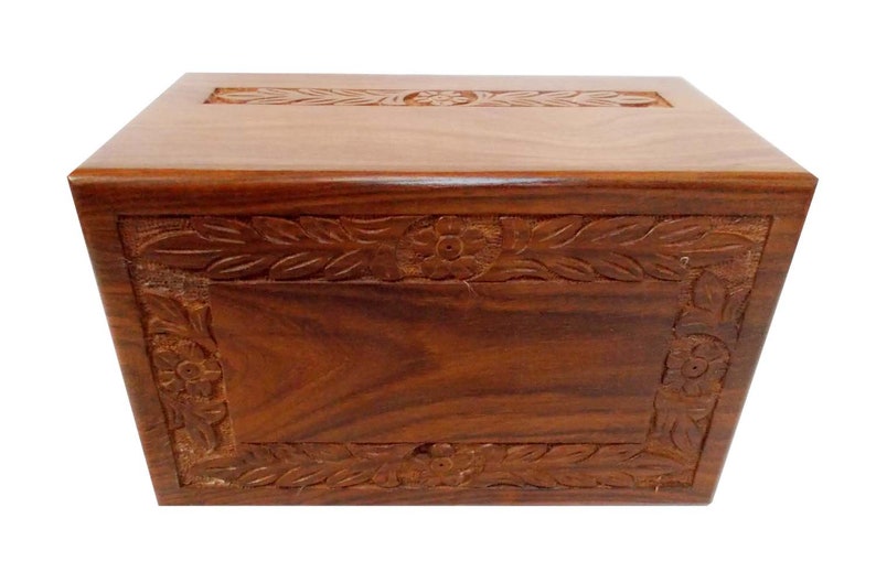 May include: A wooden cremation urn with a carved floral design. The urn is made of dark wood and has a rectangular shape.