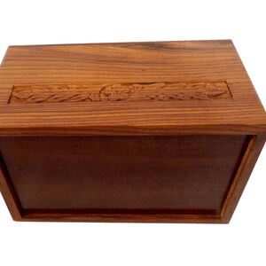 May include: A wooden box with a carved design on the top. The box is made of dark wood and has a natural finish.