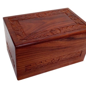 May include: A wooden cremation urn with a carved floral design. The urn is made of dark reddish-brown wood and has a rectangular shape.