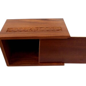 May include: A wooden box with a hinged lid. The box is made of dark brown wood and has a carved design on the top. The lid is open and the inside of the box is empty.
