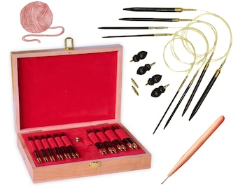 May include: A wooden box with a red velvet interior containing a set of 12 knitting needles. The needles are made of wood and have gold tips. The box is open and the needles are arranged in rows. There is a ball of yarn and a crochet hook in the background.