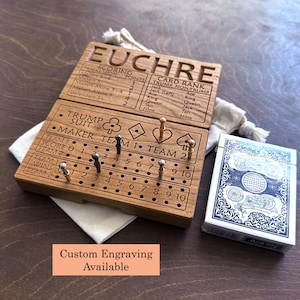 Peut inclure: Un plateau de score en bois rectangulaire pour le jeu de Euchre, gravé avec du texte, des classements de cartes et des symboles de couleurs. Il comporte des rangées de trous pour des pions métalliques afin de suivre les scores. Un jeu de cartes bleu et blanc est posé à côté.