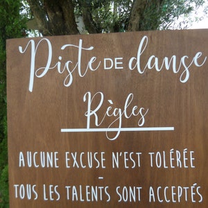 May include: A wooden sign with white text that reads "Piste de danse" and "R&egrave;gles". The sign also includes the text "Aucune excuse n'est tol&eacute;r&eacute;e" and "Tous les talents sont accept&eacute;s".