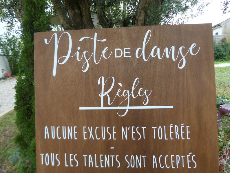 May include: A wooden sign with white text that reads "Piste de danse" and "R&egrave;gles". The sign also includes the text "Aucune excuse n'est tol&eacute;r&eacute;e" and "Tous les talents sont accept&eacute;s".