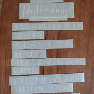 May include: Light blue vinyl stickers with white text that reads "R&egrave;gles de la Piste de danse" and includes rules for a dance floor. The rules are: "La piste de danse doit toujours &ecirc;tre occup&eacute;e", "Tous les styles et talents sont accept&eacute;s", "Chanter &agrave; tue-t&ecirc;te est vivement recommand&eacute;", "Mettre sa cravate sur la t&ecirc;te est grandement encourag&eacute;", and "Avec la b&eacute;n&eacute;diction des mari&eacute;s".