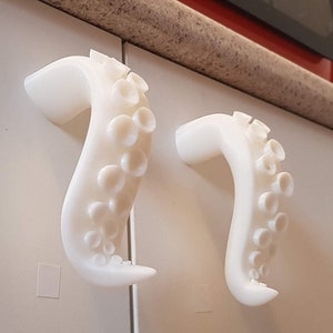 Könnte beinhalten: Zwei weiße 3D-gedruckte, krakenförmige Schrankknöpfe. Die Knöpfe sind so gestaltet, dass sie wie ein Krakenarm mit Saugnäpfen aussehen.