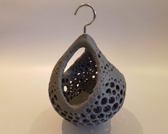 May include: A grey ceramic hanging planter with a unique, honeycomb-like design. The planter has a metal hook at the top for hanging.