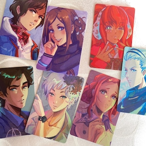 Puede incluir: Una colección de impresiones artísticas rectangulares con ilustraciones de personajes de estilo anime. Las impresiones muestran una variedad de personajes con diversos peinados, tonos de piel y expresiones. La paleta de colores incluye azules, rojos, morados y amarillos.