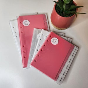 Op de afbeelding: Een set van vijf A7-formaat planner-scheidingsbladen in roze en wit. De scheidingsbladen hebben zes tabbladen met de tekst "Content List 1" op elk tabblad. De scheidingsbladen zijn verpakt in doorzichtig plastic.