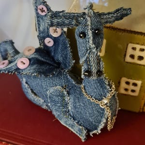 May include: A blue denim dragon toy with pink buttons and a silver chain. The dragon is sitting on a red book.