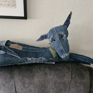 Könnte beinhalten: Ein Spielzeug für Hunde aus Jeans, hergestellt aus wiederverwendeten blauen Jeans, das auf einem dunkelgrauen Sofa liegt. Das Hundespielzeug hat einen langen, dünnen Körper und einen spitzen Kopf mit zwei schwarzen Augen.
