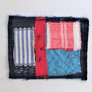 May include: A small patchwork quilt made of different fabrics, including denim, striped fabric, and red fabric. The quilt is stitched together with black thread and has a simple design.