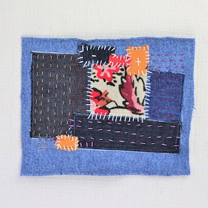 Può includere: Un patchwork di tessuto denim in tonalità di blu, nero e bianco, con un tessuto a stampa floreale al centro. I pezzi di tessuto sono cuciti insieme con cuciture visibili.