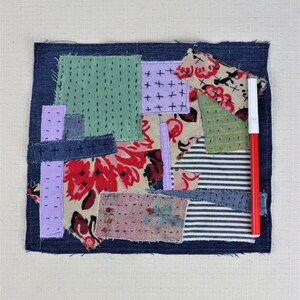 以下が含まれることがあります： デニム、花柄、ストライプ生地など、さまざまな生地で作られたパッチワークキルトの正方形。正方形は濃い青色のデニムの縁取りで囲まれています。赤いマーカーが正方形の横に置かれています。