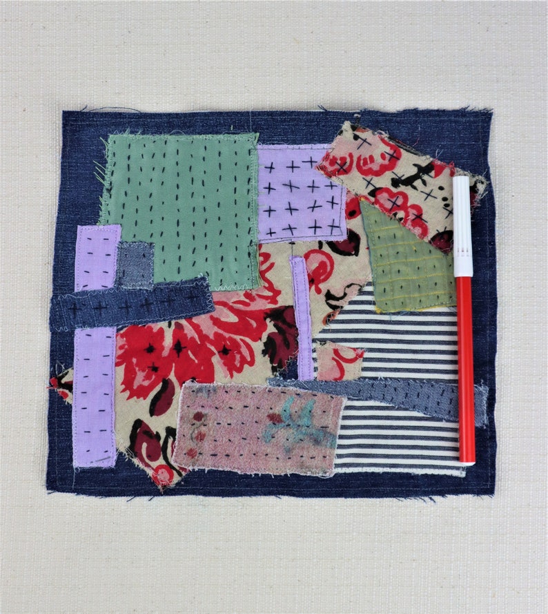 以下が含まれることがあります： デニム、花柄、ストライプ生地など、さまざまな生地で作られたパッチワークキルトの正方形。正方形は濃い青色のデニムの縁取りで囲まれています。赤いマーカーが正方形の横に置かれています。
