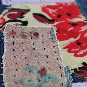 以下が含まれることがあります： デニム生地のアップで、複数のパッチが縫い付けられています。パッチは異なる生地で作られており、赤、ピンク、青の色合いの花柄が施されています。