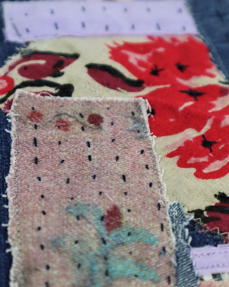 以下が含まれることがあります： デニム生地のアップで、複数のパッチが縫い付けられています。パッチは異なる生地で作られており、赤、ピンク、青の色合いの花柄が施されています。