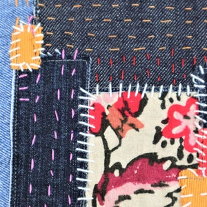 May include: A patchwork of denim fabric with different coloured stitching. The fabric is sewn together in a random pattern, creating a unique and textured look.