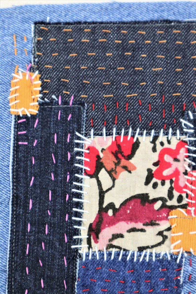 May include: A patchwork of denim fabric with different coloured stitching. The fabric is sewn together in a random pattern, creating a unique and textured look.