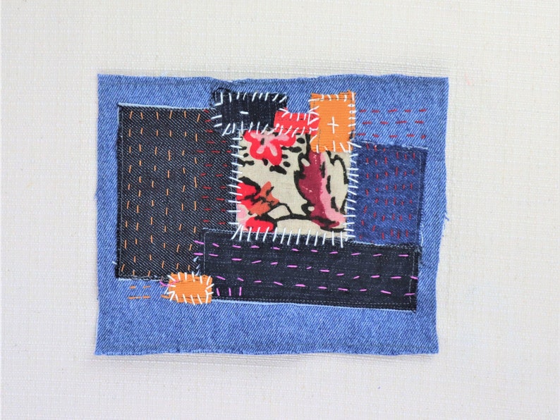 May include: A patchwork of denim fabric in shades of blue, black, and white, with a floral print fabric in the centre. The fabric pieces are sewn together with visible stitching.