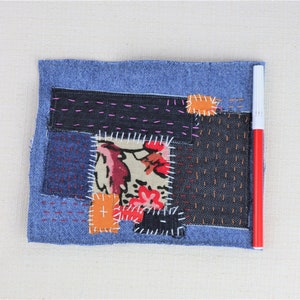 May include: A blue denim patchwork quilt featuring a variety of fabrics and stitching patterns. The quilt is made up of different coloured fabrics, including red, orange, and white. The quilt is stitched together with different coloured threads, including pink, orange, and white.