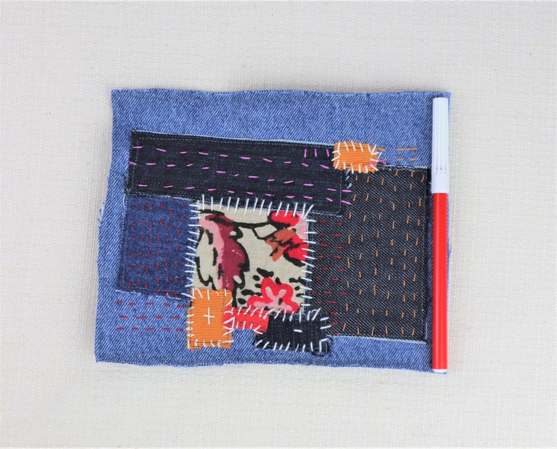 May include: A blue denim patchwork quilt featuring a variety of fabrics and stitching patterns. The quilt is made up of different coloured fabrics, including red, orange, and white. The quilt is stitched together with different coloured threads, including pink, orange, and white.