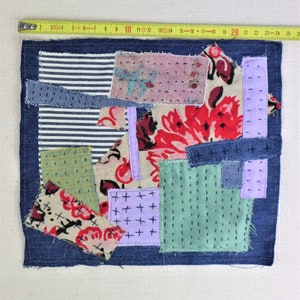 以下が含まれることがあります： デニム、花柄、ストライプなど、さまざまな生地で作られたパッチワークキルト。キルトはさまざまなステッチで縫い合わせられ、濃い青色のデニムの縁取りが施されています。