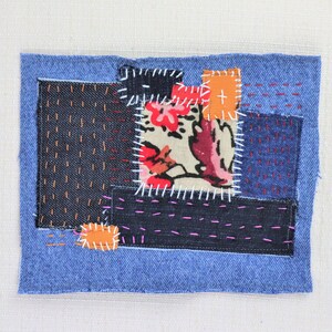 May include: A patchwork of denim fabric in various shades of blue, with a floral print fabric in the centre. The fabric pieces are sewn together with different coloured threads, creating a unique and textured design.