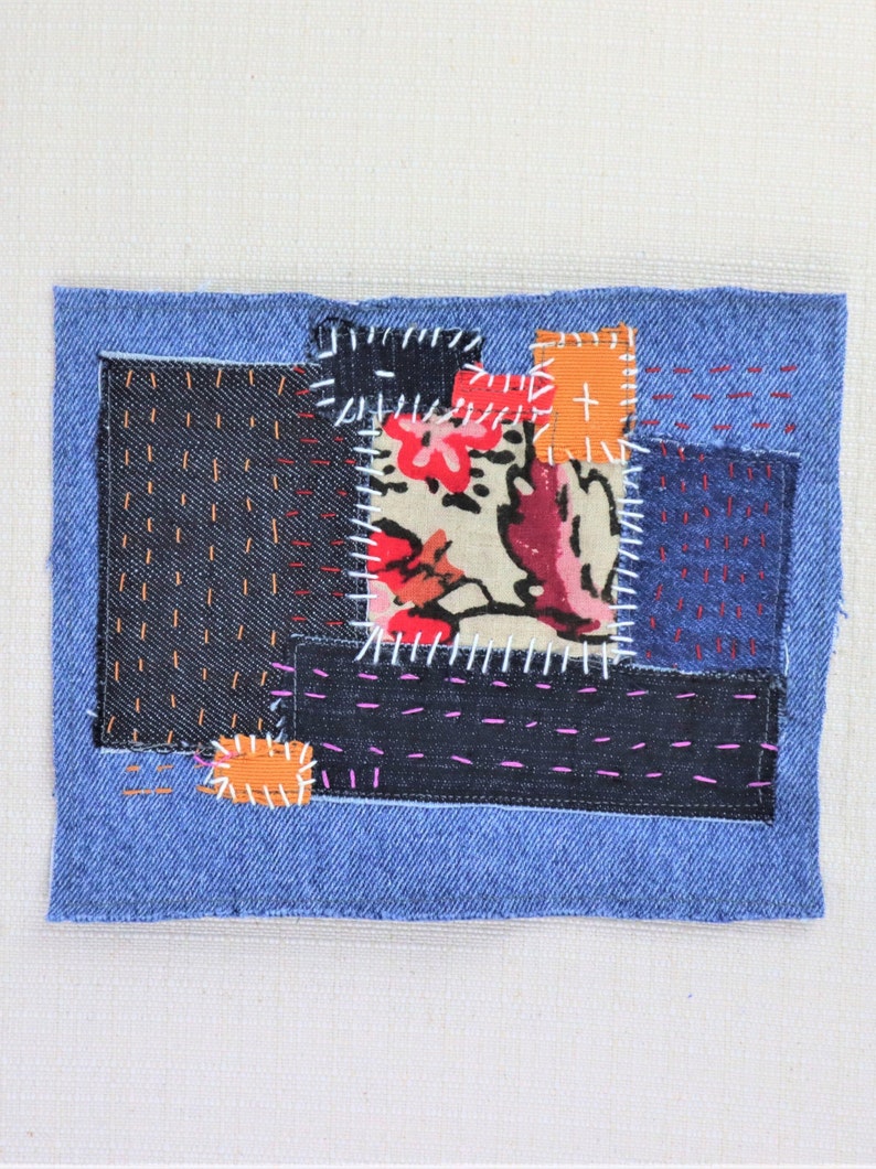 May include: A patchwork of denim fabric in various shades of blue, with a floral print fabric in the centre. The fabric pieces are sewn together with different coloured threads, creating a unique and textured design.