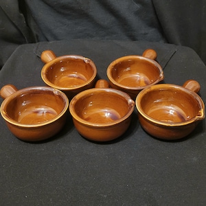 Könnte beinhalten: Satz mit fünf braunen Suppenschalen aus Keramik mit Henkeln. Die Schalen sind alle gleich groß und haben die gleiche Form und eine glänzende Oberfläche.