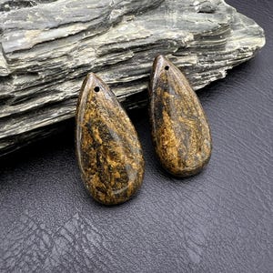 Puede incluir: Dos colgantes en forma de lágrima hechos de hierro tigre marrón y dorado. Los colgantes tienen un agujero en la parte superior para encordar.