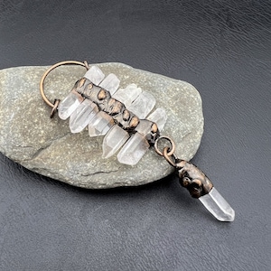 May include: A copper wire wrapped pendant with clear quartz crystals. The pendant is attached to a copper wire loop.