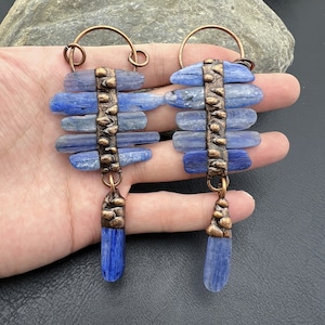 May include: A pair of blue kyanite earrings with copper wire and beads. The earrings are dangle style and have a long, teardrop shape.