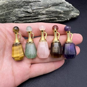 Puede incluir: Cinco botellas de piedras preciosas en miniatura con detalles dorados. Las botellas están hechas de ojo de tigre, aventurina verde, cuarzo rosa, cuarzo ahumado y amatista.