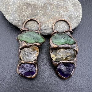 May include: A pair of earrings with a layered design featuring green, yellow, and purple stones set in bronze metal.