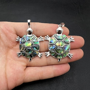 May include: Two silver turtle pendants with iridescent abalone shell inlays. The turtles have detailed carvings and a shiny finish.