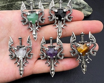 May include: A collection of silver-toned pendants featuring a sword design with heart-shaped gemstones in green, black, white, purple, and yellow. The pendants have a dragon-like design with wings.