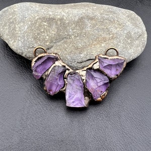 May include: A purple amethyst pendant necklace with a raw, natural crystal design. The pendant is made of five amethyst stones set in a bronze metal frame.