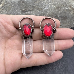 May include: Two clear quartz crystal points with red faceted glass gems set in silver tone metal settings. The crystals are approximately 2 inches long.