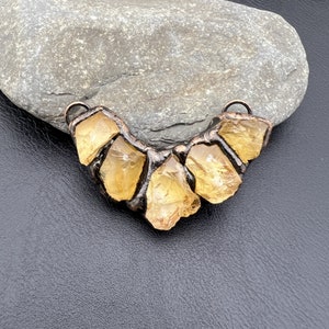 May include: A copper wire necklace with five yellow citrine stones. The stones are set in a wire frame and are arranged in a crescent shape.