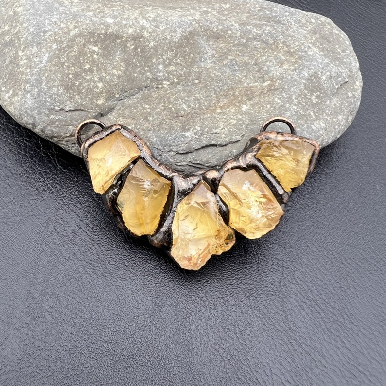 May include: A copper wire necklace with five yellow citrine stones. The stones are set in a wire frame and are arranged in a crescent shape.