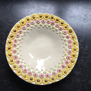 May include: A white ceramic serving bowl with a decorative border of yellow, pink, and green flowers. The bowl has a smooth, glossy finish.